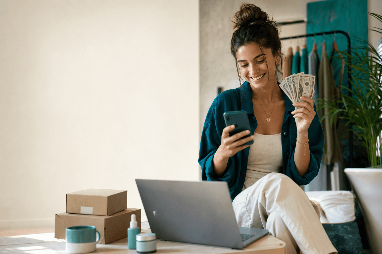 Young ecommerce creator celebrating an early sales milestone beside her laptop and parcels